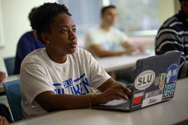 A female student sits at a desk and takes notes in a classroom.