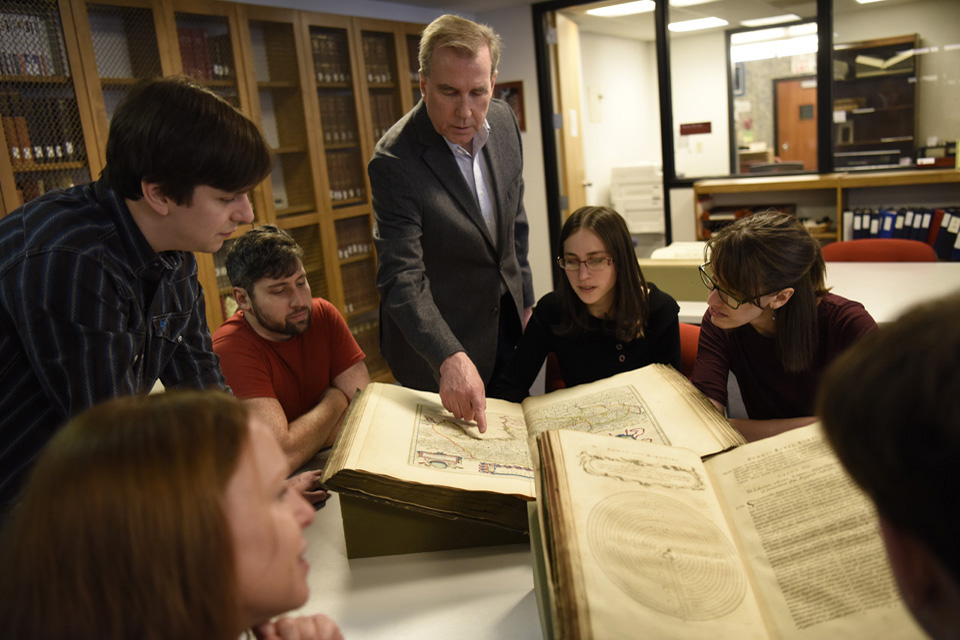 Students gathered around a book with a professor