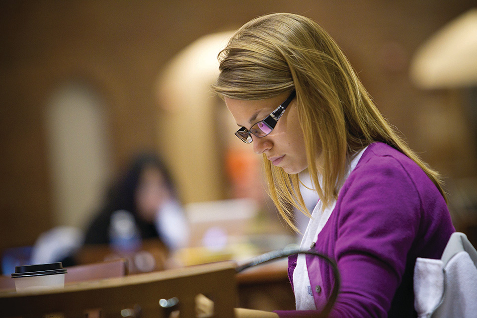 Business Student looks down at a table while working with a cup of coffee.