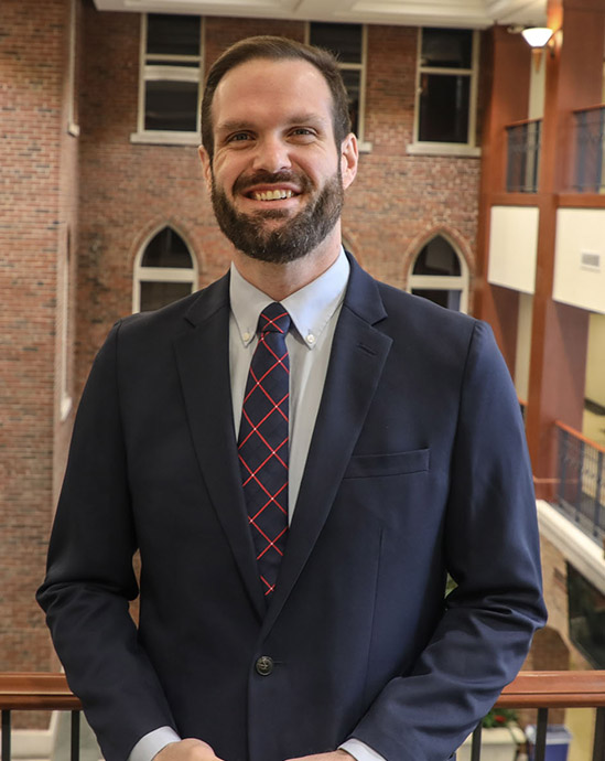 Steve Oslica smiles for the camera in Cook Hall while wearing a suit and tie