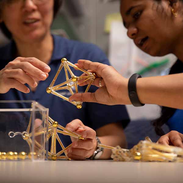 A group of students play with magnetic rods in a classroom as part of a demonstration of 3D shapes.