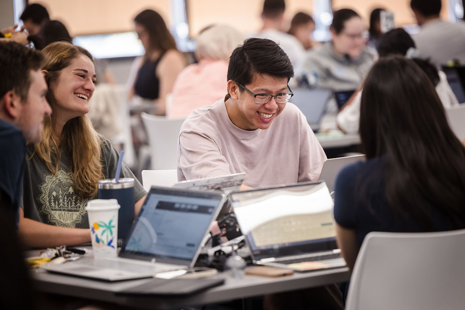 Students sit around a table with laptops studying.