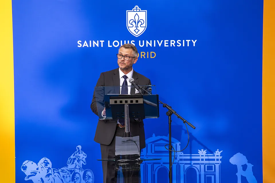 Man at podium talking to the audience, with a blue background.