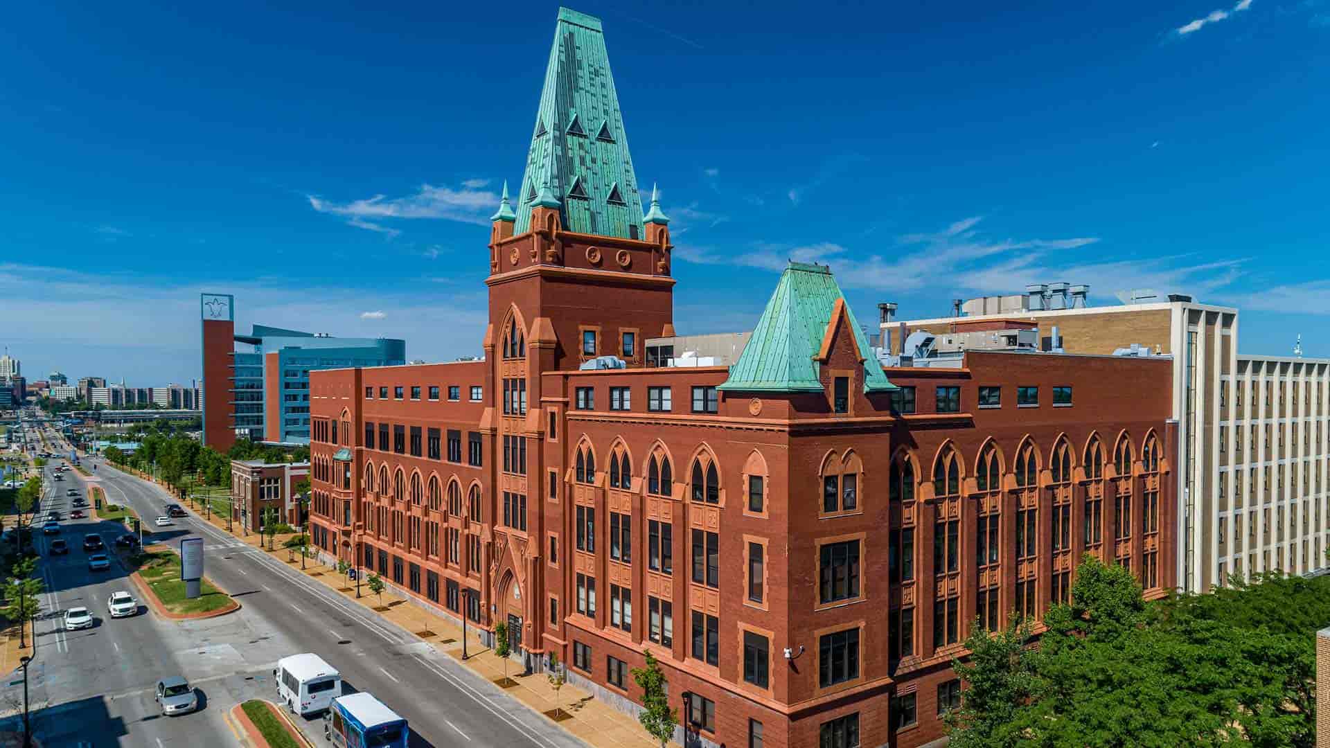 An aerial view of the exterior of Schitalla Hall, a large red-brick building with a green copper roof.