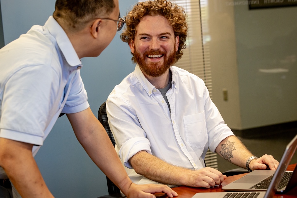 Two male CORE staff members work together on a computer at an office desk.