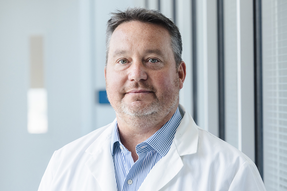 Rich DiPaolo, Ph.D., is shown in his lab. He wears a white lab coat. 