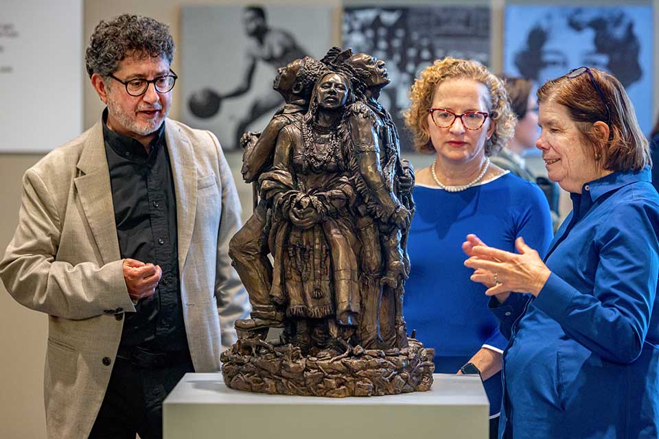 Fran Pestello, Ph.D., right,  Edward Ibur, executive director of the St. Louis Literary Award, left, and Cathleen Fleck, Ph.D., chair of the Department of Visual and Performing Arts, center, discuss the sculpture “Land, Labor, Legacy” by Kyle and Kelly Phelps with on Monday, April 28, 2025. Photo by Sarah Conroy.