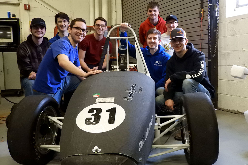 Members of the Parks Racing FSAE club pose with their black and white race car.