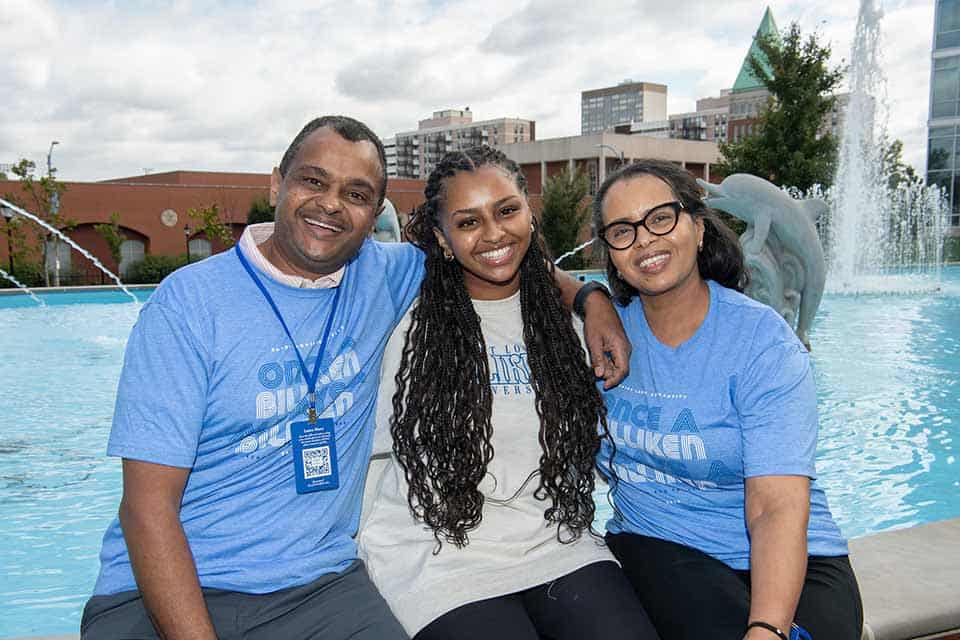 A Billiken student sits on the ledge of a SLU fountain between her parents 