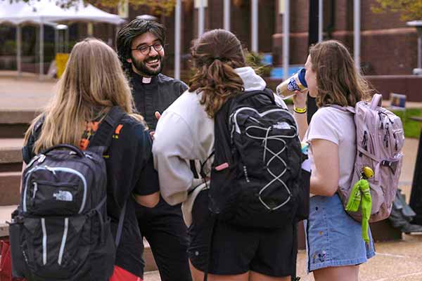 A young Jesuit wearing a priest’s collar speaks to students in the plaza close to the clock tower.